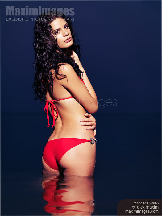 Stock photo of Beautiful glamorous woman in red bikini standing in water at night Buy commercial use license at MaximImages