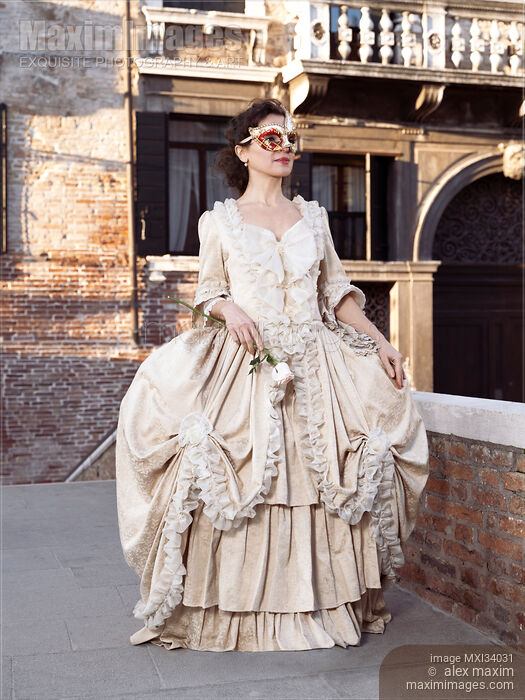 Stock photo of Beautiful lady in Venetian carnival costume dress and mask walking along historic street in Venice Buy commercial use license at MaximImages