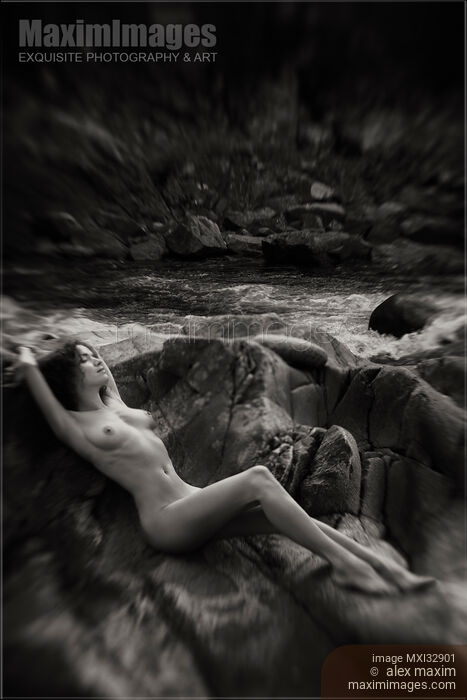 Stock photo of Beautiful nude woman lying on rocks by a river in nature scenery Black and white art nudes Buy commercial use license at MaximImages