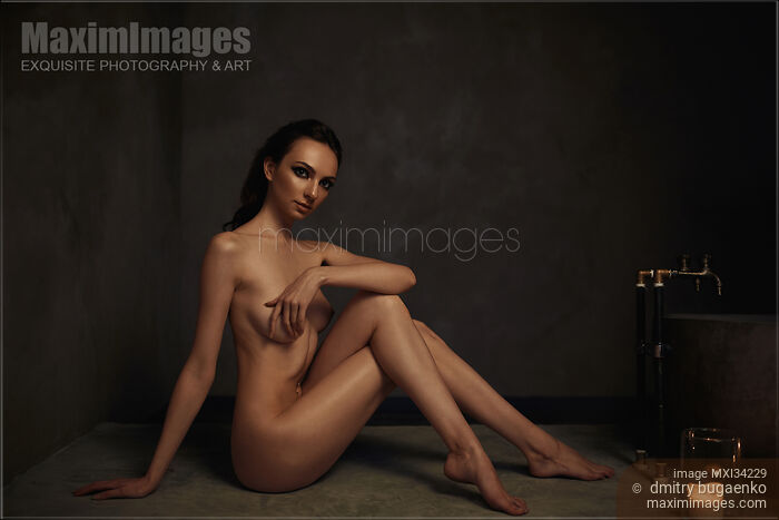 Stock photo of Beautiful nude woman sitting in a sensual pose in a dark bathroom Buy commercial use license at MaximImages