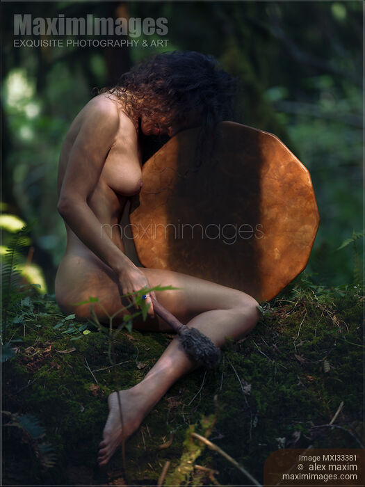 Stock photo of Beautiful nude woman sitting in a tranquil nature scenery leaning against a shamanic leather drum Buy commercial use license at MaximImages