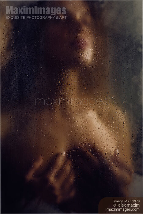Stock photo of Beautiful nude woman with her hands holding her breasts behind a wet hazy glass in dark Buy commercial use license at MaximImages