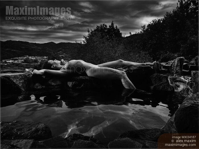 Stock photo of Beautiful nude woman with wet sexy naked body lying on rocks on the edge of onsen hot spring pool. Black and white photograph. Buy commercial use license at MaximImages