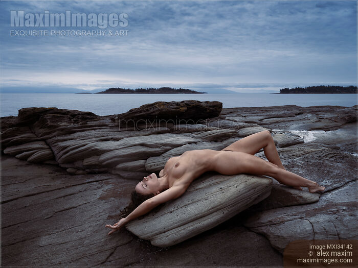 Beautiful nude young woman lying naked stretched on ocean shore rock in graceful relaxed pose in nature scenery Stock photo of Beautiful nude young woman lying naked stretched on ocean shore rock in graceful relaxed pose in nature scenery Buy commercial use license at MaximImages