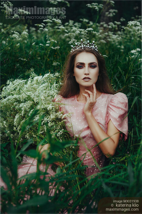 Beautiful princess in a crown sitting in a field of wild yarrow with flowers in her hands Stock photo of Beautiful princess in a crown sitting in a field of wild yarrow with flowers in her hands Buy commercial use license at MaximImages