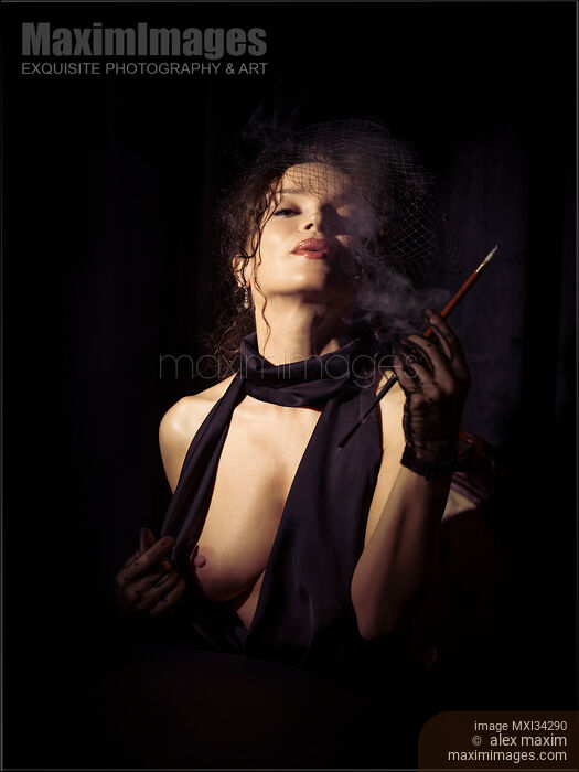 Stock photo of Beautiful seductive femme fatale lady in black dress and veil exposing her breast and exhaling cigarette smoke Buy commercial use license at MaximImages