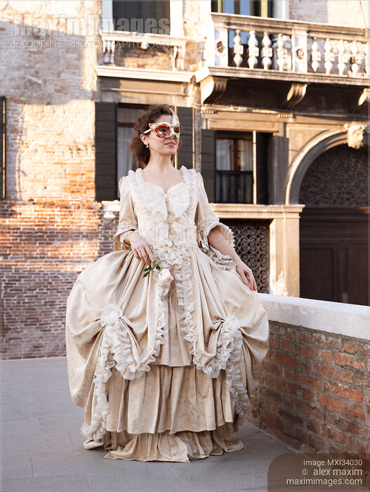 Stock photo of Beautiful smiling lady in vintage Italian carnival costume dress and mask walking along historic street in Venice Buy commercial use license at MaximImages