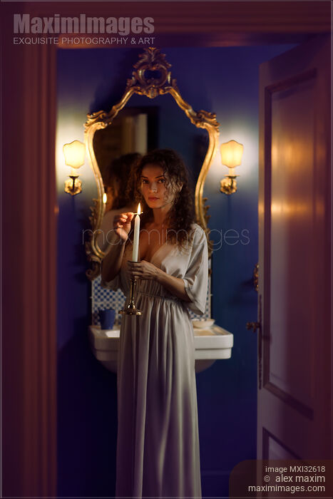 Beautiful woman in evening gown lighting a candle in her hand with an expressive mysterious look in bathroom settings Stock photo of Beautiful woman in evening gown lighting a candle in her hand with an expressive mysterious look in bathroom settings Buy commercial use license at MaximImages