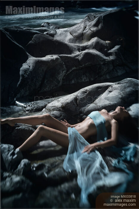 Stock photo of Beautiful woman lying on smooth river rocks with her barely covered sensual body in dramatic outdoor nature scenery Buy commercial use license at MaximImages
