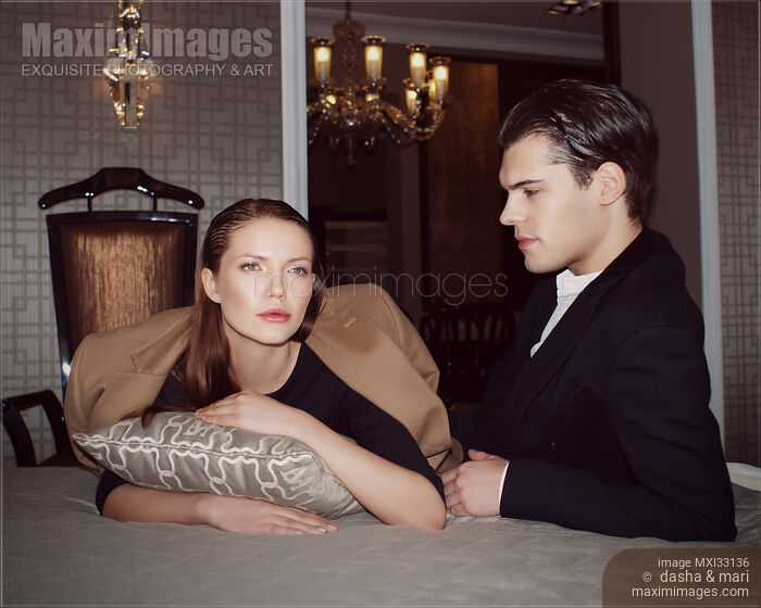 Stock photo of Beautiful young romantic couple in elegant classic clothes lying on a bed in a luxury hotel suite Buy commercial use license at MaximImages