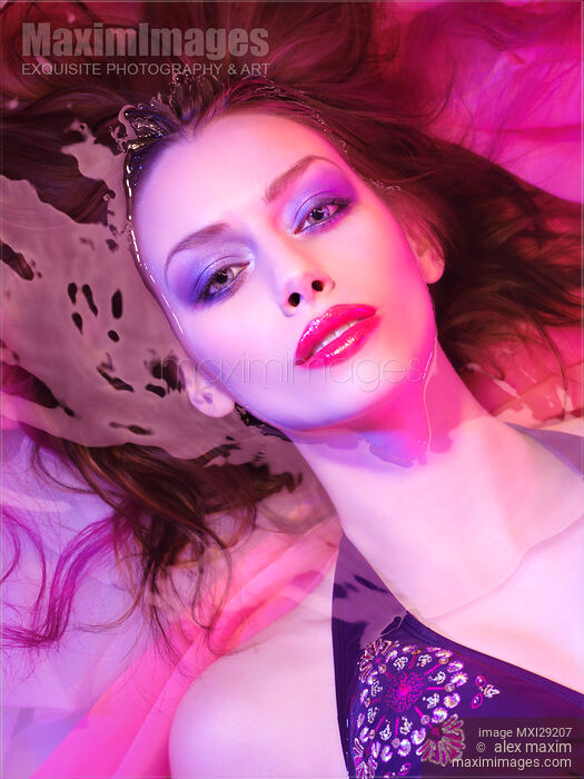 Stock photo of Beauty face portrait of woman lying in water with makeup in vivid pink purple colored light Buy commercial use license at MaximImages