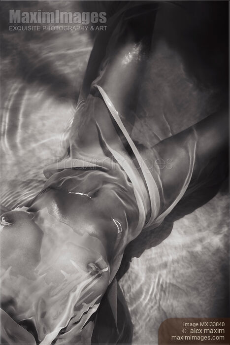 Stock photo of Black and white sensual nude woman body wrapped with wet sheer cloth in glossy water revealing her breasts and parted legs Buy commercial use license at MaximImages