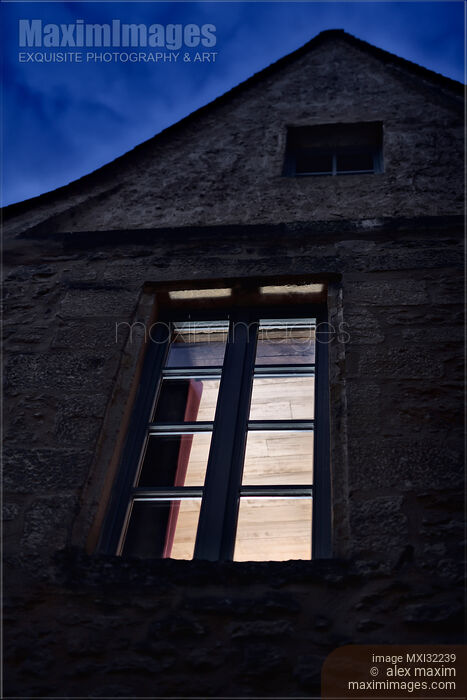 Closed window of an old French stone house under dark twilight skies with light inside Stock photo of Closed window of an old French stone house under dark twilight skies with light inside Buy commercial use license at MaximImages