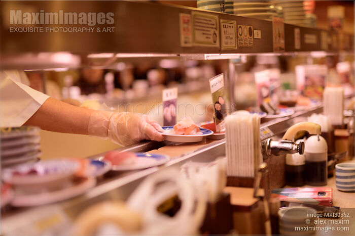 Stock photo of Closeup of a sushi chef placing a plate on a conveyor belt at Musashi Sushi restaurant in Kyoto Buy commercial use license at MaximImages
