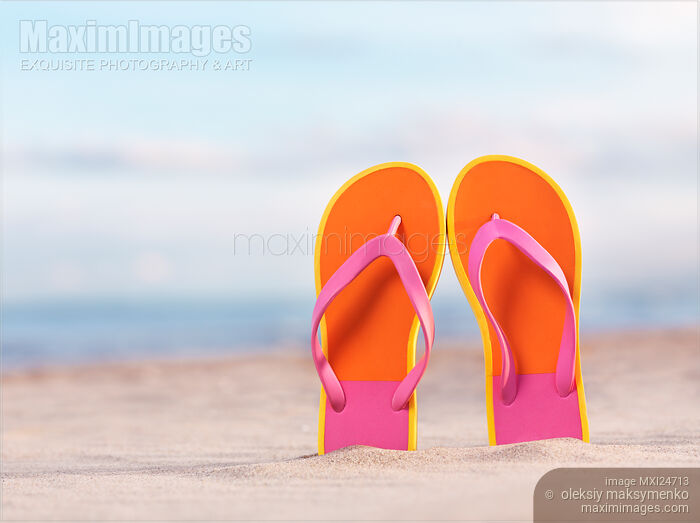 Stock photo of Colorful orange flip flops in sand at the beach Buy commercial use license at MaximImages