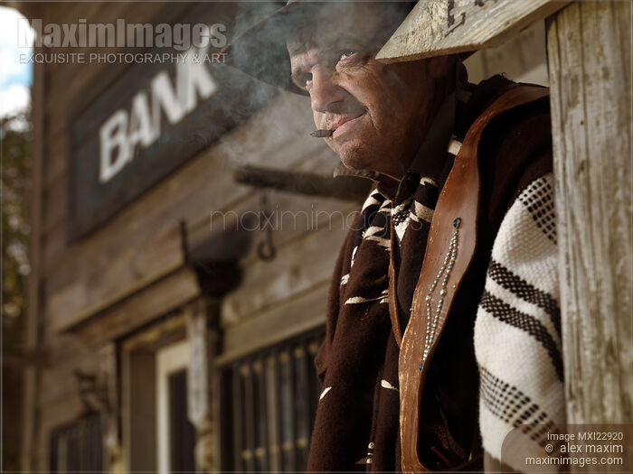Stock photo of Cowboy Smoking a Cigar Outside of a Bank Building Notorious villain in Wild west style Buy commercial use license at MaximImages
