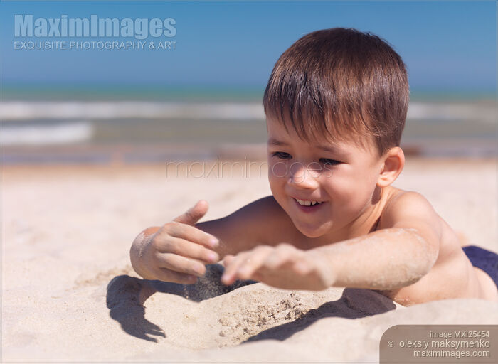 Stock photo of Cute happy little boy playing in the sand on the beach Buy commercial use license at MaximImages