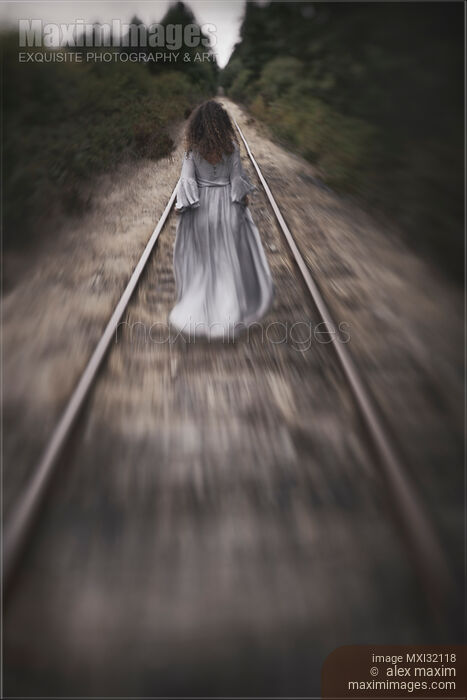 Stock photo of Dramatic concept of a woman in a long dress walking away along railroad tracks Buy commercial use license at MaximImages