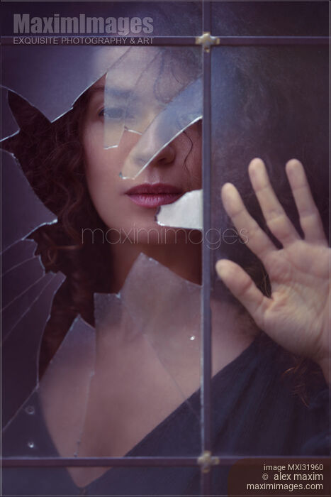 Stock photo of Dramatic conceptual portrait of a woman face behind a broken window pane glass Buy commercial use license at MaximImages
