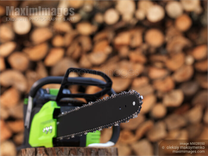 Stock photo of Electric Cordless Chainsaw by stacked firewood Buy commercial use license at MaximImages