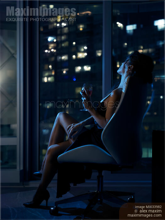 Elegant woman sitting relaxed in chair with glass of wine by window with night city view Stock photo of Elegant woman sitting relaxed in chair with glass of wine by window with night city view Buy commercial use license at MaximImages