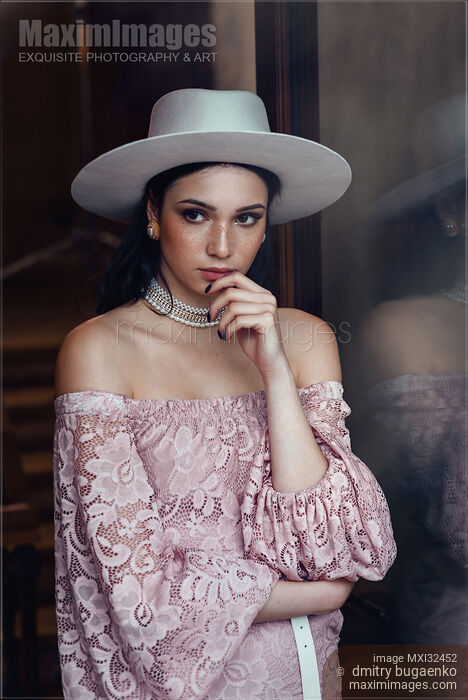 Stock photo of Elegant young woman in pink lace dress and white hat with a thoughtful expression Buy commercial use license at MaximImages