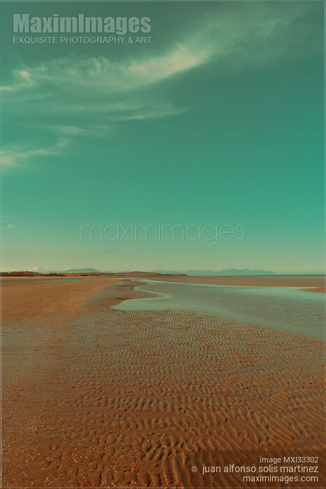 Empty sea beach at low tide in sunrise with wave patterns in the sand under blue sky Stock photo of Empty sea beach at low tide in sunrise with wave patterns in the sand under blue sky Buy commercial use license at MaximImages