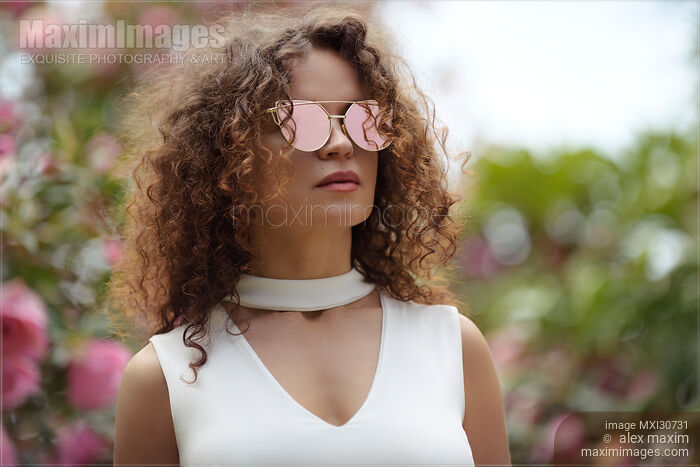 Fashion portrait of a beautiful young woman wearing cat-eye sunglasses and a white v-neck top Stock photo of Fashion portrait of a beautiful young woman wearing cat-eye sunglasses and a white v-neck top Buy commercial use license at MaximImages