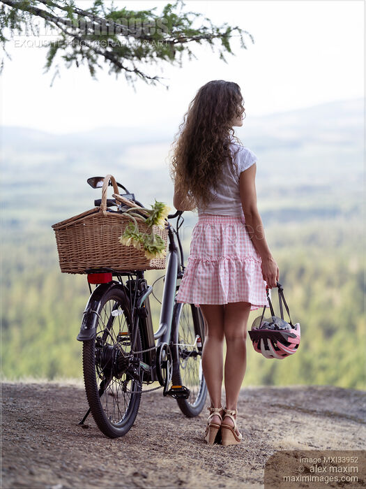 Girl with an electric bike and a pink bicycle helmet enjoying the nature view from a cliff Stock photo of Girl with an electric bike and a pink bicycle helmet enjoying the nature view from a cliff Buy commercial use license at MaximImages