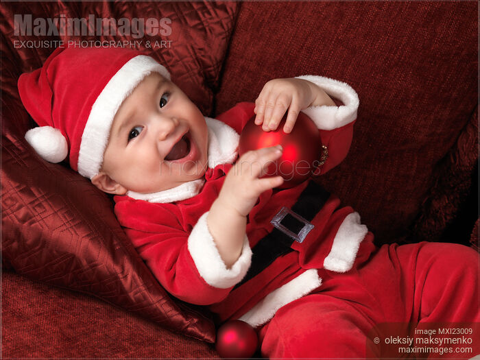 Stock photo of Happy Baby Boy in Santas Costume with a Christmas Bauble Buy commercial use license at MaximImages