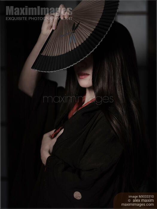 Stock photo of Japanese woman in black kimono and red lips covering with a hand fan. Mysterious asian lady portrait. Buy commercial use license at MaximImages