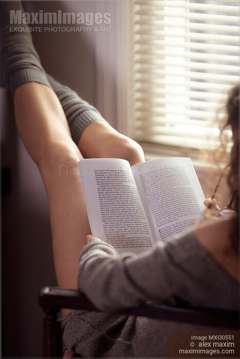 Stock photo of Legs of a woman reading a book in a chair by the window Buy commercial use license at MaximImages