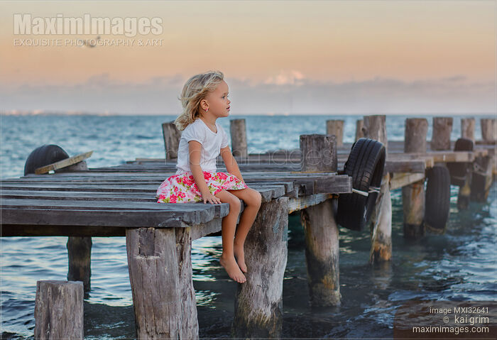 Stock photo of Little girl sitting on a wooden pier at the sea Buy commercial use license at MaximImages