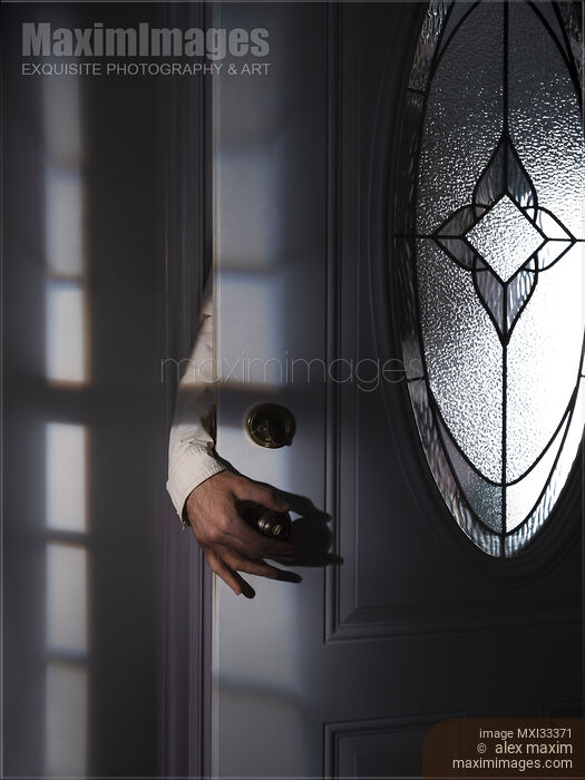Stock photo of Man hand reaching for a door handle from behind a dark shadowy house entrance door Buy commercial use license at MaximImages