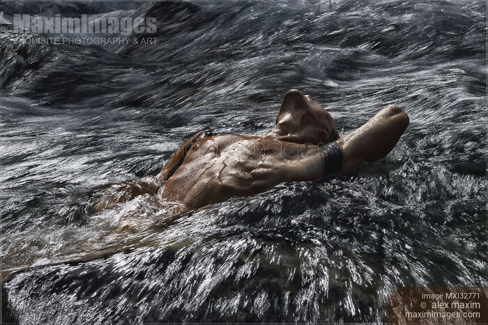 Stock photo of Man with bare wet torso lying half submerged in rushing river water Dramatic moody photograph Buy commercial use license at MaximImages