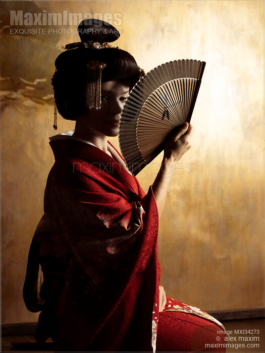 Mesmerizing portrait of beautiful caucasian lady, Japanese geisha with hand fan casting shadows on her face against golden wall Stock photo of Mesmerizing portrait of beautiful caucasian lady, Japanese geisha with hand fan casting shadows on her face against golden wall Buy commercial use license at MaximImages