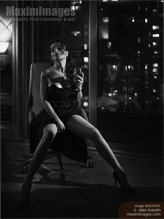 Stock photo of Noir portrait of a gorgeous lady sitting in chair in provocative pose by window with night city view Buy commercial use license at MaximImages