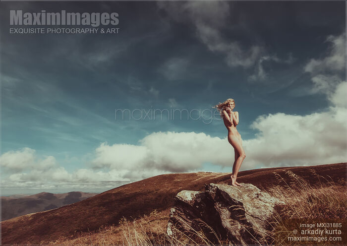 Stock photo of Nude woman standing gracefully on rocks in mountain landscape scenery with blue skies Buy commercial use license at MaximImages