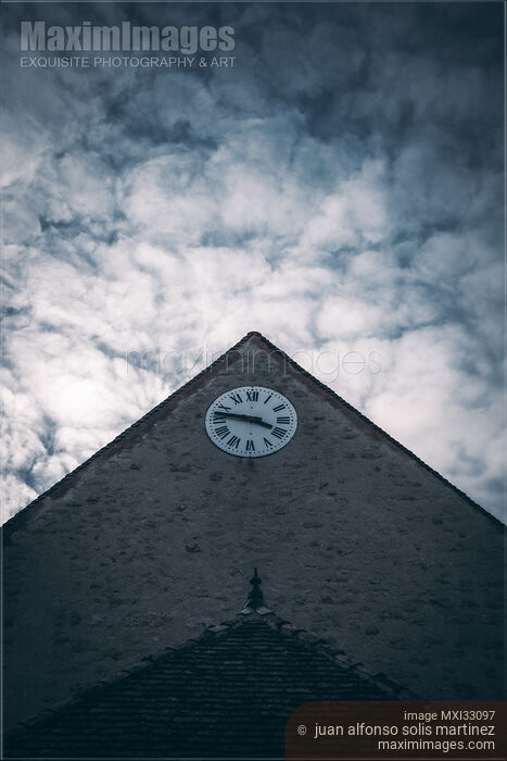 Stock photo of Old church house with a clock under dramatic sky in France Buy commercial use license at MaximImages