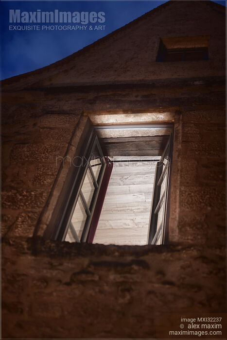 Stock photo of Open window of an old stone house illuminated from inside at night artistic concept Buy commercial use license at MaximImages