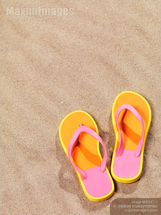 Stock photo of Pair of bright orange flip flops on beach sand Buy commercial use license at MaximImages