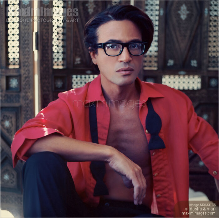 Stock photo of Portrait of a man in an undone stylish red shirt and glasses sitting relaxed in a retro style room Buy commercial use license at MaximImages