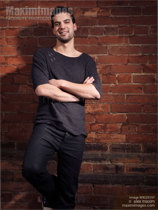 Stock photo of Portrait of a smiling young man at brick wall Buy commercial use license at MaximImages