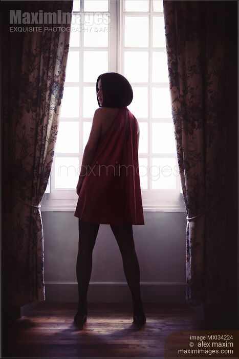 Stock photo of Rear view of a sexy lady in red mini dress and black stockings standing in a dark room by the window Buy commercial use license at MaximImages