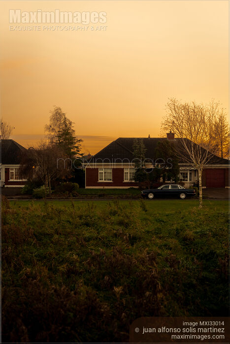 Stock photo of Residential house on a street with a parked classic car in dramatic sunset scenery Buy commercial use license at MaximImages
