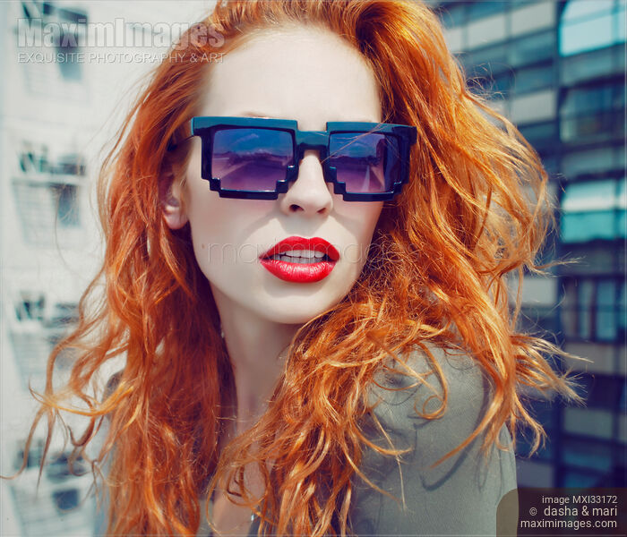 Retro fashion portrait of a young red-haired lady in funky avant-garde sunglasses on a city rooftop Stock photo of Retro fashion portrait of a young red-haired lady in funky avant-garde sunglasses on a city rooftop Buy commercial use license at MaximImages