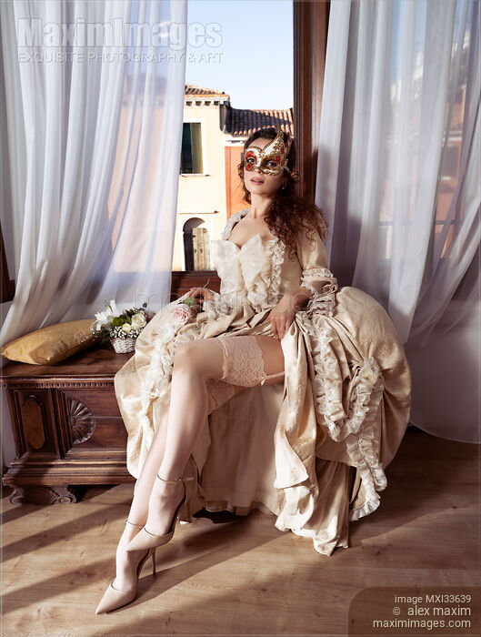 Stock photo of Seductive Venetian lady in carnival mask and beautiful vintage dress revealing her sexy legs in stockings at masquerade ball Buy commercial use license at MaximImages