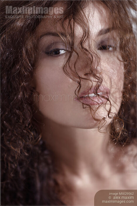 Sensual beauty face portrait of a young woman looking through her curly hair Stock photo of Sensual beauty face portrait of a young woman looking through her curly hair Buy commercial use license at MaximImages