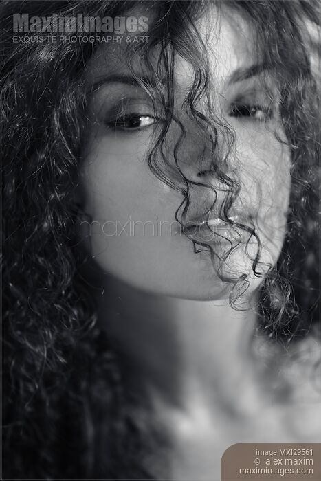 Sensual black and white beauty face portrait of a young woman looking through her curly hair Stock photo of Sensual black and white beauty face portrait of a young woman looking through her curly hair Buy commercial use license at MaximImages