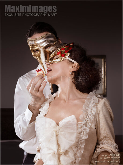 Sensual couple portrait of masked Casanova man seducing beautiful lady in vintage Venetian dress and carnival mask with cake pastry Stock photo of Sensual couple portrait of masked Casanova man seducing beautiful lady in vintage Venetian dress and carnival mask with cake pastry Buy commercial use license at MaximImages